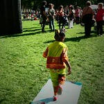 a black child plays on the hopscotch, with people and stage behind
