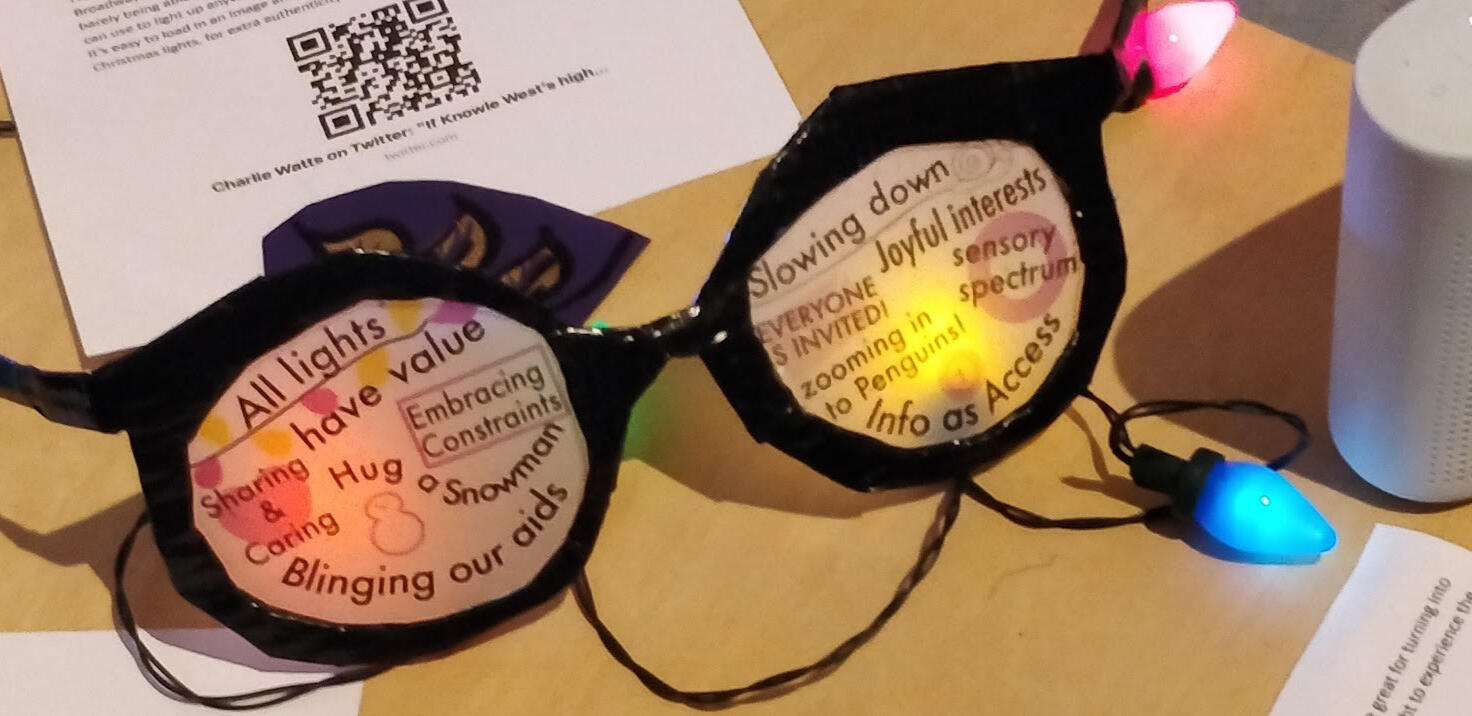The glasses have black duct tape frames and printed vellum paper lenses with different wisdoms printed on and red and yellow lights shining behind them.