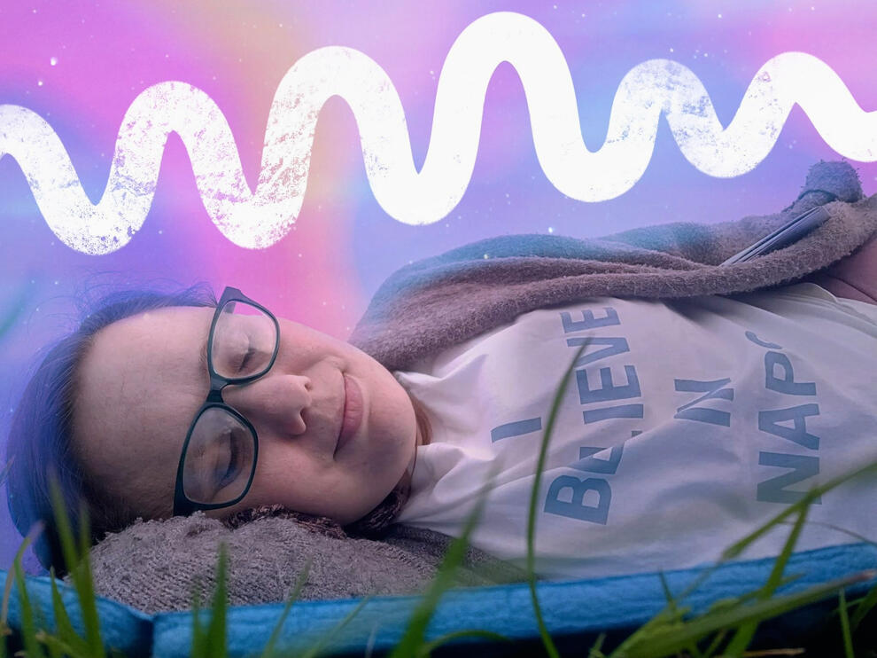 I am led with my eyes closed on my blue mat with grass stands, a pink gradient sky design and white 'recharging' squiggy and my top says 'I believe in naps'